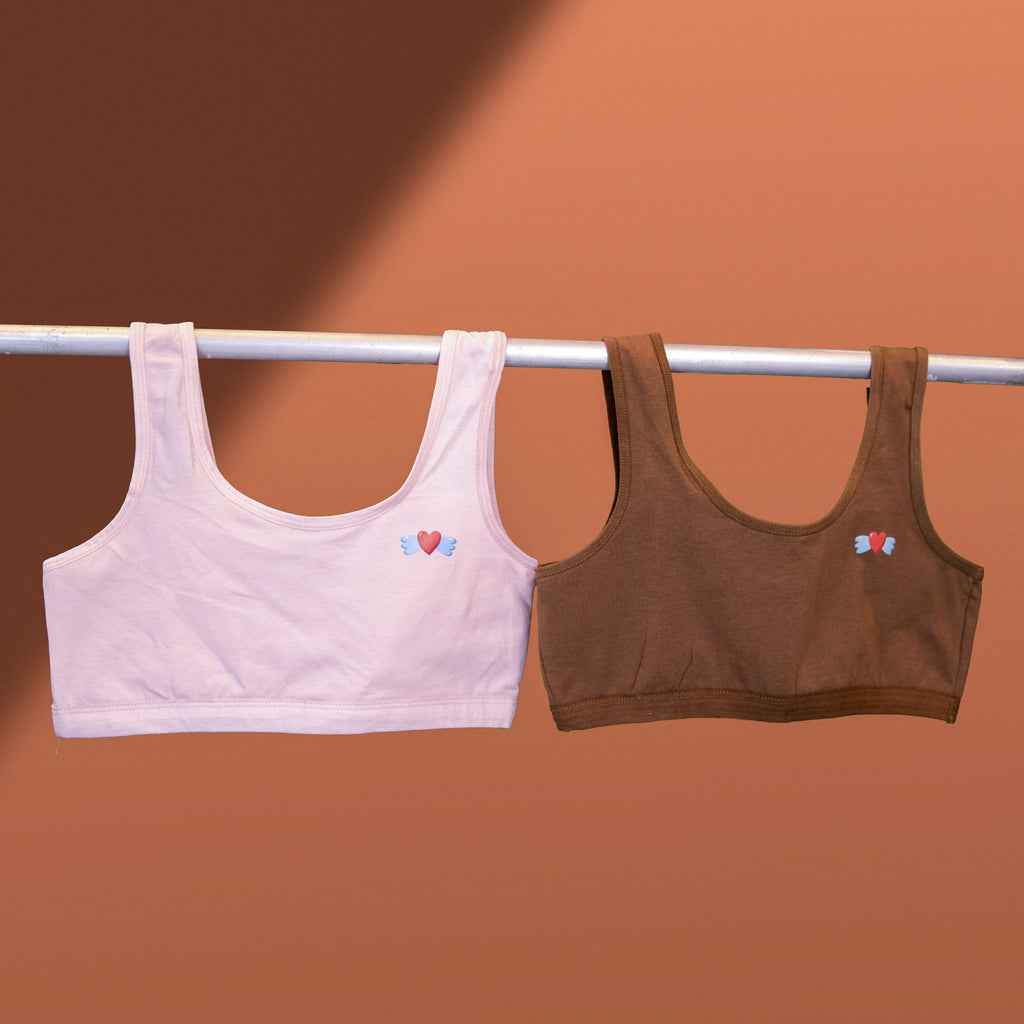 Two Charmella Slip-On Bras, hanging on a rod against a brown background.