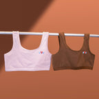 Two Charmella Slip-On Bras, hanging on a rod against a brown background.